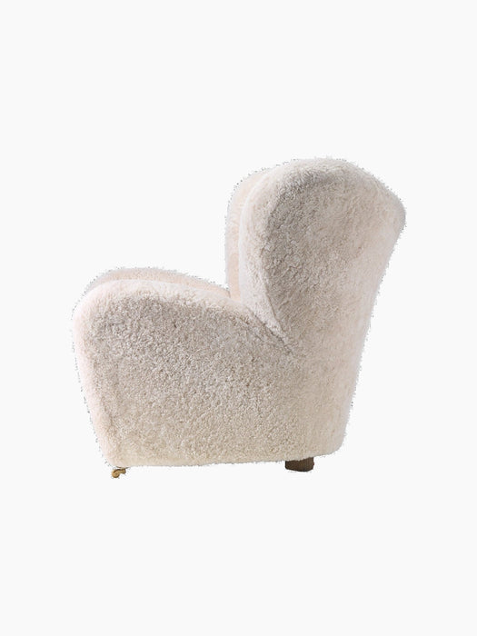 Side view of The Tired Man Lounge Chair upholstered in fluffy off-white sheepskin, showing its curved shape and wooden legs.