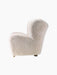 Side view of The Tired Man Lounge Chair upholstered in fluffy off-white sheepskin, showing its curved shape and wooden legs.