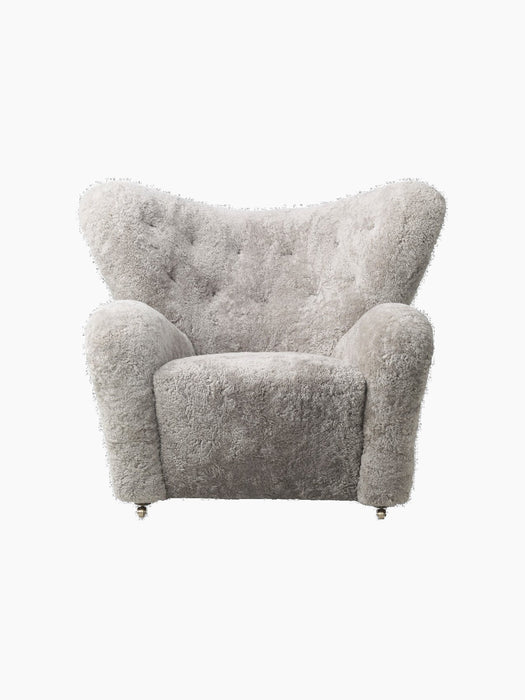 The Tired Man Lounge Chair in Sheepskin Green Tea. A plush armchair with a curved, tufted back and front brass casters.