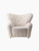 Front view of The Tired Man Lounge Chair upholstered in off-white sheepskin. Features a high, winged back and brass casters.