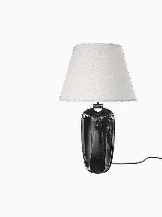 The Torso Table Lamp, 57, shown at an angle, featuring a glossy black stoneware base and a textured, off-white linen shade.
