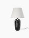 The Torso Table Lamp, 57, shown at an angle, featuring a glossy black stoneware base and a textured, off-white linen shade.