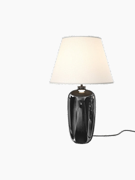 Torso Table Lamp, 57 with a glossy black ceramic base and an off-white linen shade, illuminated against a black background.