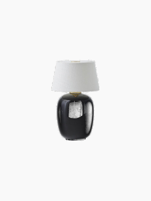 A studio shot of the black Torso Portable Table Lamp, featuring a glossy, rounded ceramic base and a white linen lampshade.
