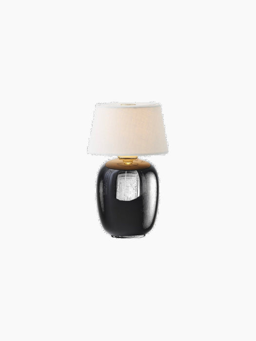 The Torso Table Lamp, Portable, illuminated. It features a glossy black ceramic base and an off-white linen canvas shade.