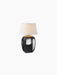 The Torso Table Lamp, Portable, illuminated. It features a glossy black ceramic base and an off-white linen canvas shade.