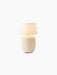A lit Torso Portable Table Lamp in Sand, featuring a textured ceramic base and linen lampshade against a black background.