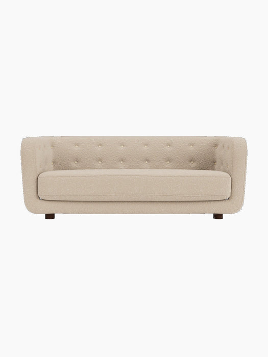 Front view of the Vilhelm Sofa, upholstered in light beige Sahco Zero 1 fabric with button details and dark smoked oak legs.