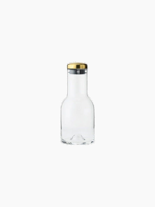 A 0.5L clear glass water bottle with a cylindrical neck and curved body, sealed with a polished brass lid on a black base.