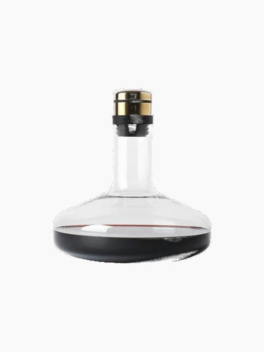 A glass Wine Breather Deluxe decanter with a wide base and brass stopper, containing red wine, against a black background.
