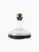 A glass Wine Breather Deluxe decanter with a wide base and brass stopper, containing red wine, against a black background.