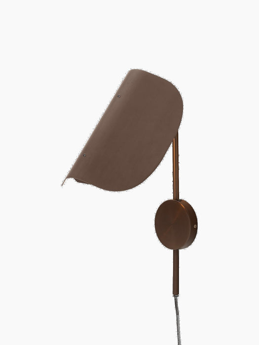 Angled view of the bronzed aluminium Wing Wall Lamp with its light on, highlighting the distinctive wing-shaped shade.