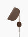 Angled view of the bronzed aluminium Wing Wall Lamp with its light on, highlighting the distinctive wing-shaped shade.