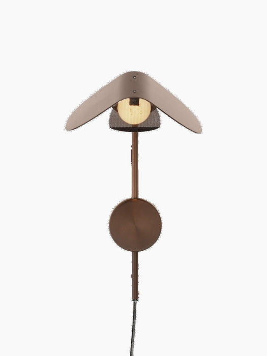 Front view of the turned-on Wing Wall Lamp in Bronzed Aluminium, featuring its wing-shaped shade over a glowing bulb.